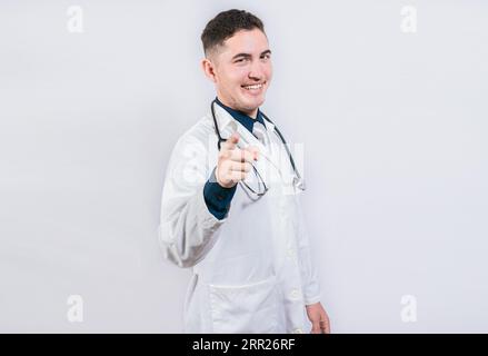 Gut aussehender Arzt, der auf die Kamera zeigt. Freundlicher und lächelnder Arzt zeigt auf Sie, junger Arzt zeigt auf Sie Stockfoto