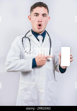 Schockierter Arzt, der eine Anwendung auf das Handy zeigt. Staunte der junge Arzt, der den Handy-Bildschirm hält und zeigt Stockfoto