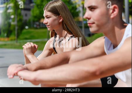 Junge sportliche Männer und Frauen, die zusammen trainieren und auf einem Trainingsplatz unter freiem Himmel hocken. Stockfoto