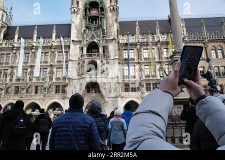 Ein Tourist nutzt ein Telefon, um auf dem Marienplatz das Glockenspiel im neuen Rathaus zu sehen. Marienplatz, München, Deutschland Stockfoto