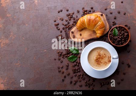 Tasse schwarzer Kaffee und Croissant auf braunem Steinhintergrund mit Kaffeebohnen und Blättern, Kopierraum Stockfoto