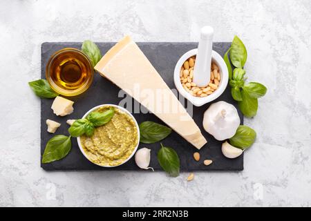 Pesto-Sauce und Zutaten, Schwarzes Käseplatten, Basilikum, Knoblauch, Pinienkerne, Olivenöl auf grauem Steinhintergrund mit Kopierraum Stockfoto