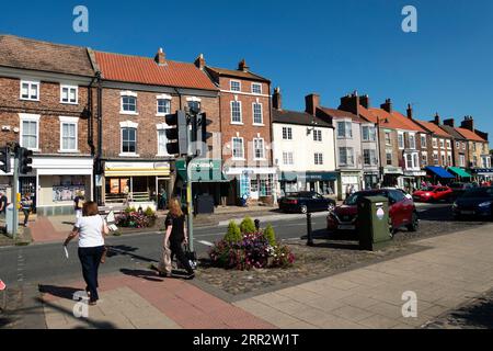 Die High Street der Marktstadt Stokesley North Yorkshire an einem sonnigen Sommertag mit zwei Damen, die auf die Straßenüberquerung warten Stockfoto