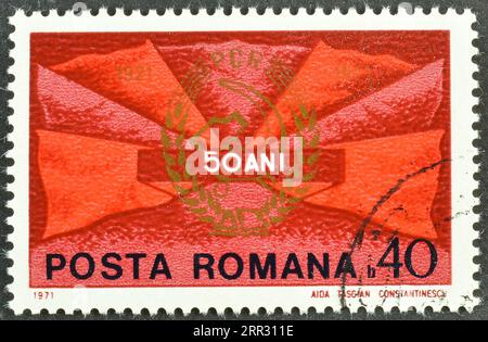 Von Rumänien gedruckte, stornierte Briefmarke, die rote Flaggen und das Abzeichen der Kommunistischen Partei zeigt, 50. Jahrestag der rumänischen Kommunistischen Partei, um 1971. Stockfoto