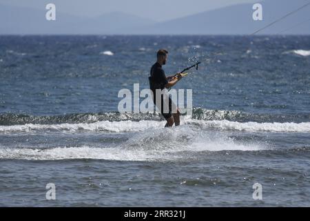 Meereslandschaft mit malerischer Aussicht auf einen jungen Kitesurfer, der eine Welle vor der Küste von Artemida in Attika, Griechenland, reitet. Stockfoto