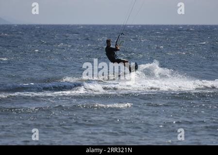 Meereslandschaft mit malerischer Aussicht auf einen jungen Kitesurfer, der eine Welle vor der Küste von Artemida in Attika, Griechenland, reitet. Stockfoto