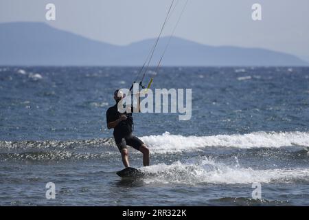 Meereslandschaft mit malerischer Aussicht auf einen jungen Kitesurfer, der eine Welle vor der Küste von Artemida in Attika, Griechenland, reitet. Stockfoto