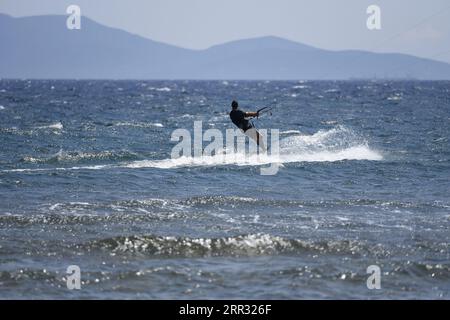 Meereslandschaft mit malerischer Aussicht auf einen jungen Kitesurfer, der eine Welle vor der Küste von Artemida in Attika, Griechenland, reitet. Stockfoto