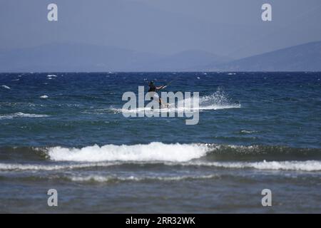 Meereslandschaft mit malerischer Aussicht auf einen jungen Kitesurfer, der eine Welle vor der Küste von Artemida in Attika, Griechenland, reitet. Stockfoto