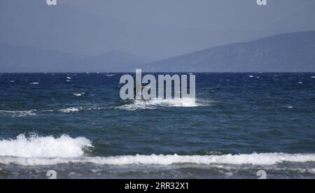 Meereslandschaft mit malerischer Aussicht auf einen jungen Kitesurfer, der eine Welle vor der Küste von Artemida in Attika, Griechenland, reitet. Stockfoto