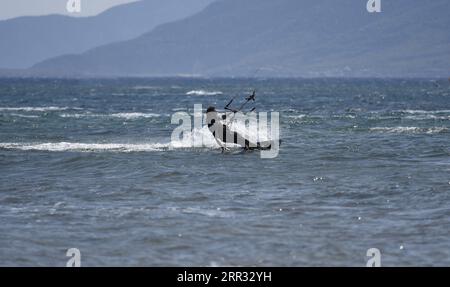 Meereslandschaft mit malerischer Aussicht auf einen jungen Kitesurfer, der eine Welle vor der Küste von Artemida in Attika, Griechenland, reitet. Stockfoto