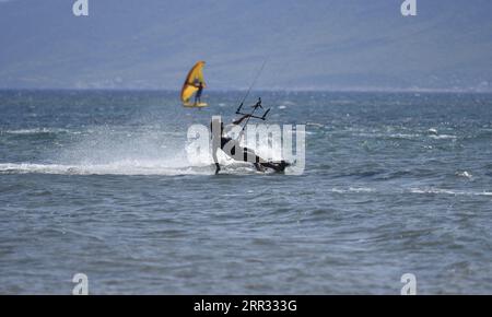 Meereslandschaft mit malerischer Aussicht auf einen jungen Kitesurfer, der eine Welle vor der Küste von Artemida in Attika, Griechenland, reitet. Stockfoto