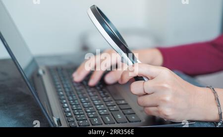 Frau, die Arbeit macht und eine Lupe benutzt, um sich Daten anzusehen, die für Infografiken geeignet sind. Stockfoto