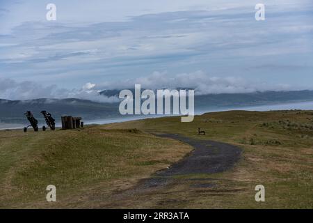 Ein gewundener Schotterweg durchquert eine üppige, grasbewachsene Landschaft und führt zu einem felsigen Hügel Stockfoto