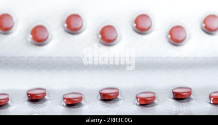 Rote Pillen in roher Anordnung. Fokuslinie im Vordergrund. Pharmazeutische Verpackungsherstellung. Stockfoto