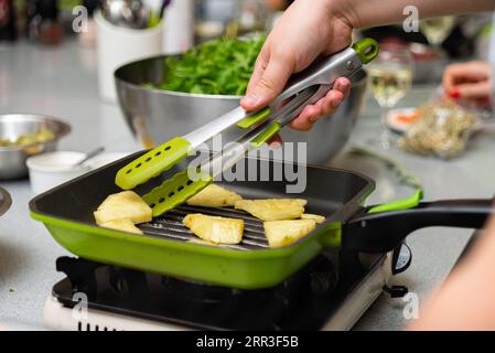 Nahaufnahme einer Frau, die eine Zange hält und Ananasscheiben auf einer Grillpfanne umdreht Stockfoto