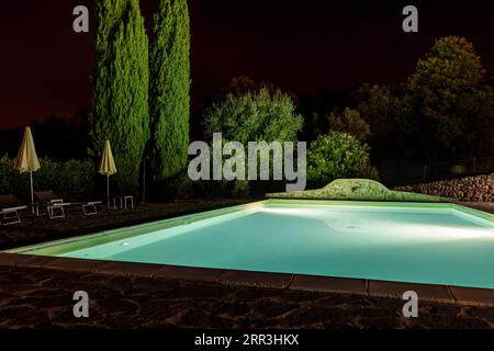 Beleuchteter Swimmingpool auf dem Hügel von Montemassi, umgeben von Zypressen und Oleandern in der Provinz Grosseto. Italien Stockfoto