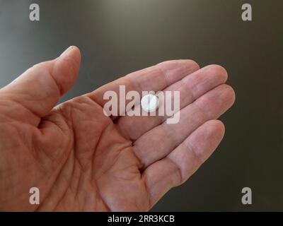 Männliche Hand hält eine Pille in der Hand auf grauem Hintergrund, nimmt Ihre Medikamente. Schließen Stockfoto