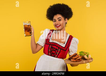 Fröhliche afroamerikanische oktoberfest-Kellnerin mit Bier und Essen auf Holztablett auf gelbem Banner Stockfoto