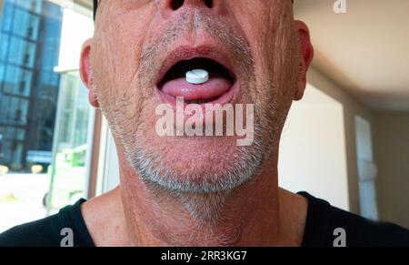Der Mann nimmt Medikamente. Weiße Pille auf Zunge bei reifem Mann mit Stoppeln. Nahaufnahme. Stockfoto