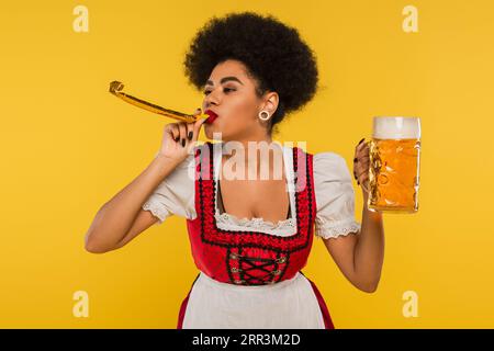 afroamerikanische oktoberfest-Kellnerin mit Partyhorn und Becher Craft-Schaumbier auf Gelb Stockfoto