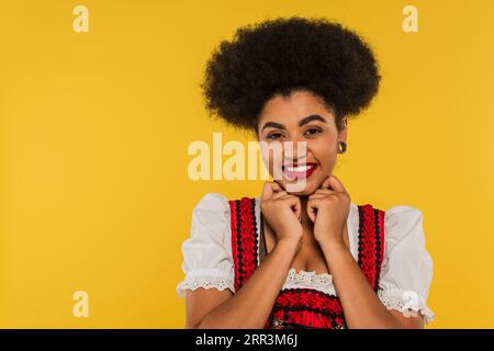 afroamerikanische oktoberfest-Kellnerin im traditionellen Dirndl, die die Kamera auf gelb anschaute Stockfoto