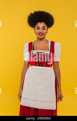 Freute afroamerikanische Kellnerin in authentischer bayerischer Tracht auf gelbem oktoberfest-Konzept Stockfoto