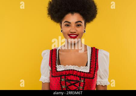 Attraktive afroamerikanische bayerische Kellnerin in traditionellem Kostüm mit Blick auf die Kamera auf Gelb Stockfoto