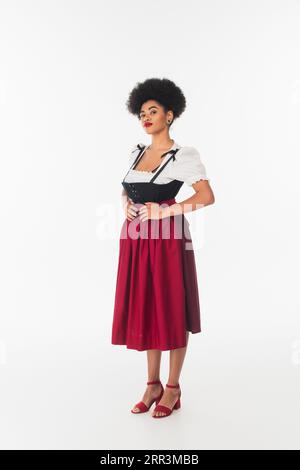 Selbstbewusste afroamerikanische oktoberfest-Kellnerin in traditioneller bayerischer Tracht, die auf weiß steht Stockfoto