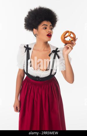 Staunte afroamerikanische bayerische Kellnerin in oktoberfestkleidung und sah leckere Brezel auf weiß Stockfoto