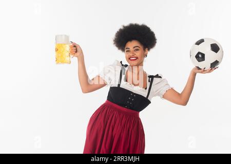 Fröhliche afroamerikanische oktoberfest-Kellnerin mit einem Becher Bier mit Schaum und Fußball auf weiß Stockfoto