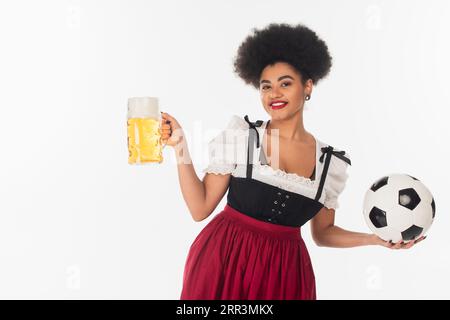 afroamerikanische oktoberfest-Kellnerin mit Fußballball und Becher Lagerbier mit Schaum auf weiß Stockfoto