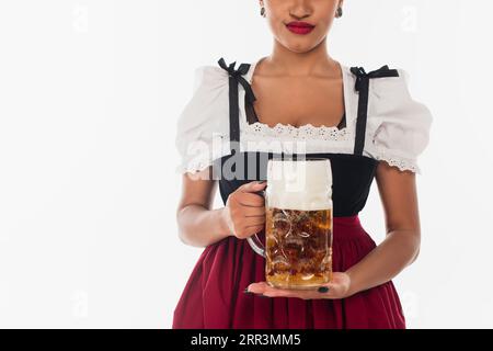 Zugeschnittene afroamerikanische bayerische Kellnerin im Dirndl mit einem Becher Bier auf weiß, oktoberfest Stockfoto