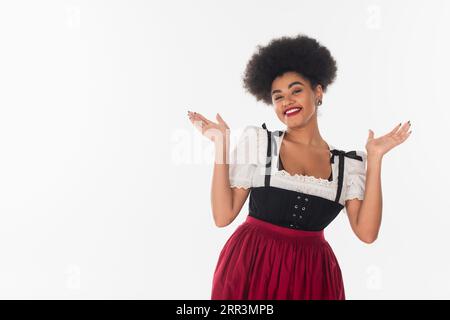 Fröhliche afroamerikanische bayerische Kellnerin in traditioneller Tracht, die zum oktoberfest auf weiß einlädt Stockfoto