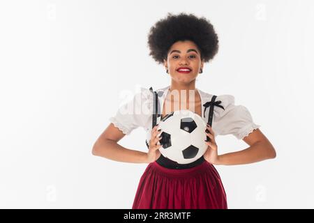 afroamerikanische bayerische Kellnerin im Dirndl mit Fußballball auf weiß, oktoberfest-Konzept Stockfoto