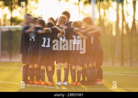 Jugendsportler stehen in einem Kreis, der sich vor dem Spiel zusammenkauert und sich gegenseitig motiviert. Kinder, die Mannschaftssportspiele im Sommer spielen Stockfoto