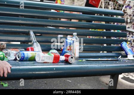 Leere Plastikflaschen und Bierdosen als Müll in und um die öffentliche Bank auf der Straße. Stockfoto