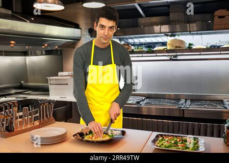 Der lachende Koch im kleinen Bistro bereitet köstlichen Burger in der belebten Küche zu. Stockfoto