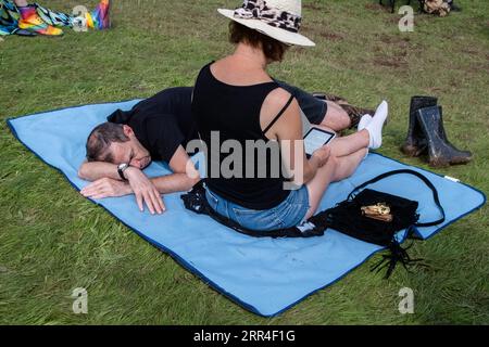 Ein Mann mittleren Alters, der ein Nickerchen macht, während sein Partner ein kindle beim Green man Festival liest, Brecon, Wales, Großbritannien, 2023. Foto: Rob Watkins Stockfoto