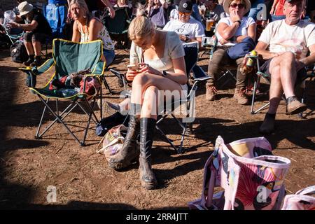 Eine junge Frau, die auf ihrem Handy mit matschigen Stiefeln beim Green man Festival, Brecon, Wales, Großbritannien, 2023 scrollt. Foto: Rob Watkins Stockfoto