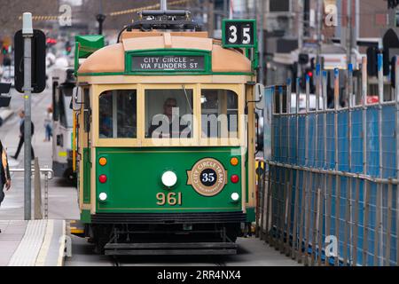 35 Melbourne Tram, eine Vintage Tram der W-Klasse auf dem Stadtkreis, die in eine Straßenbahnhaltestelle fährt, mit der Skyline von Melbourne im Hintergrund. Stockfoto