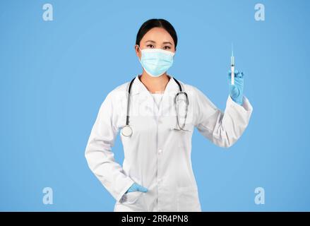 Immunisierungskonzept. Selbstbewusste asiatische Ärztin, die medizinische Schutzmaske trägt, die Spritze hält Stockfoto