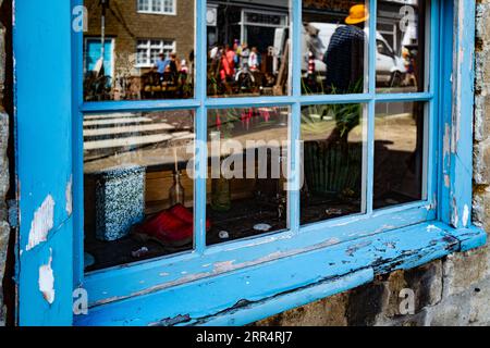 Antiquitäten hinter einem verwitterten blauen Fensterrahmen. Konzept von bunt, seelenvoll, Retro, künstlerisch, Stil, Grunge, antik. Zusammenfassung. Stockfoto