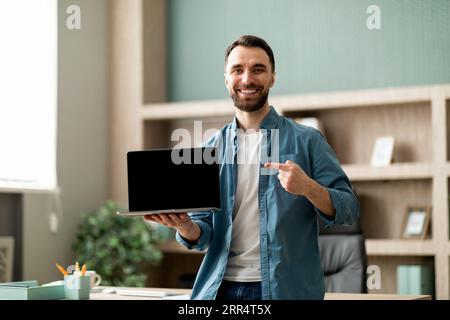 Geschäftsmann Zeigt Mit Dem Finger Auf Den Leeren Laptop, Während Er In Der Nähe Des Schreibtisches Im Büro Steht Stockfoto