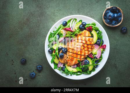 Köstlicher Salat mit Blaubeeren, gegrilltem Huhn, Avocado, roter Zwiebel, Walnüssen, Rucola und gemischte Kräuter, grüner Tischhintergrund, Draufsicht Stockfoto