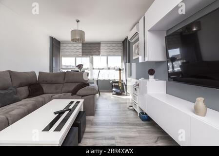 Ein Wohnzimmer mit weißen Holzmöbeln, weißen und grauen Wänden, Holzfußboden und einem großen Fenster auf der Rückseite. Stockfoto