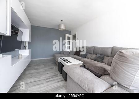 Ein Wohnzimmer mit weißen Holzmöbeln, weißen und grauen Wänden, hellen Holzfußböden, einem großen grauen Stoffsofa und einer silbernen Lampe Stockfoto
