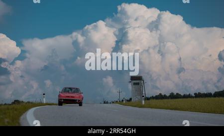 Der alte GT-Oldtimer fährt auf einer Landstraße mit majestätischen Wolken im Hintergrund auf die Kamera zu. Magische Wolkenkulisse. Stockfoto