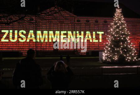 201223 -- PEKING, 23. Dez. 2020 -- Besucher schauen sich das Schloss Bellevue an, das durch eine Lichtprojektion des deutschen Wortes „zusammenkleben“ in Berlin, Hauptstadt Deutschlands, 17. Dez. 2020, beleuchtet wird. Xinhua Schlagzeilen-Yearender: Eine Welt, die sich angesichts der verheerenden Pandemie ShanxYuqi PUBLICATIONxNOTxINxCHN schneller entwickelt Stockfoto