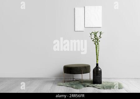 Vase mit grünen Bambusstämmen und Pouf in der Nähe von hellen Wänden Stockfoto